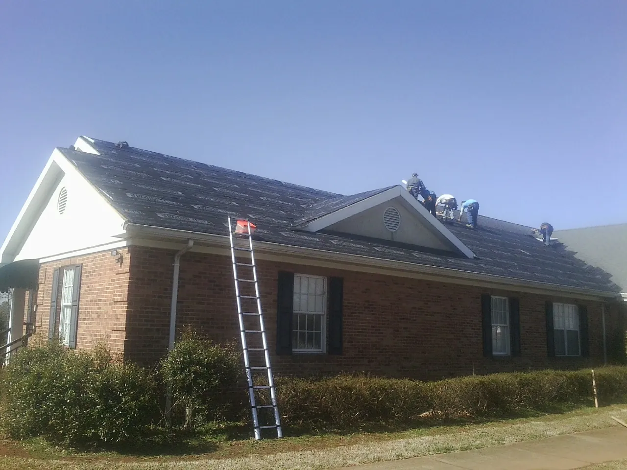 Crew tearing shingles off a brick ranch roof with a ladder set — Metal Roof Repair work by our crew in Fresh Meadows