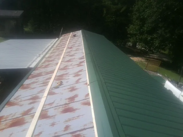 Old rusted panels beside newly installed green metal roofing — Wind Damage Roof Repair by Roofing Brothers in Fresh Meadows