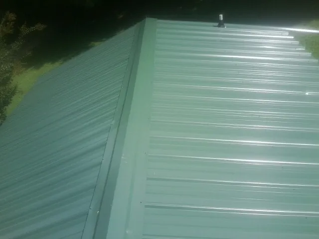 New green metal panels meeting at the ridge of a roof — Flat Roof Repair work by our crew in Fresh Meadows