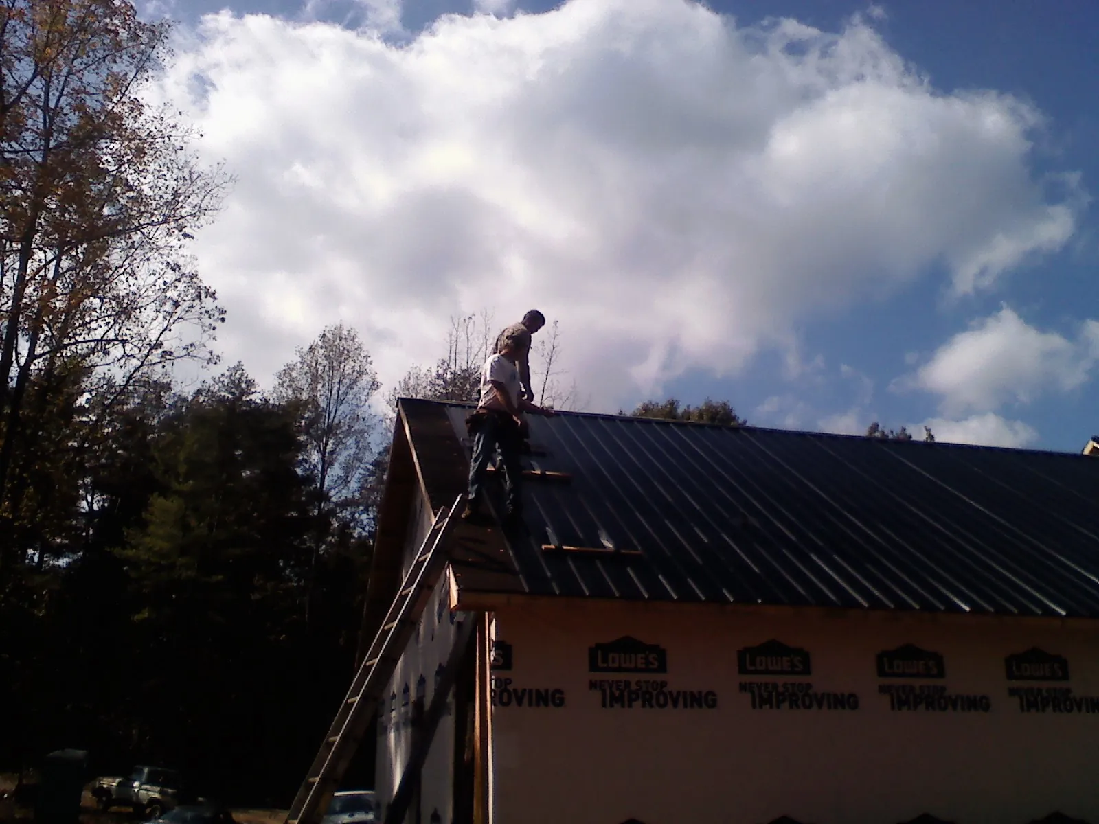 Roofer fastening dark metal panels high against a cloudy sky, from a Roof Inspection job in Fresh Meadows
