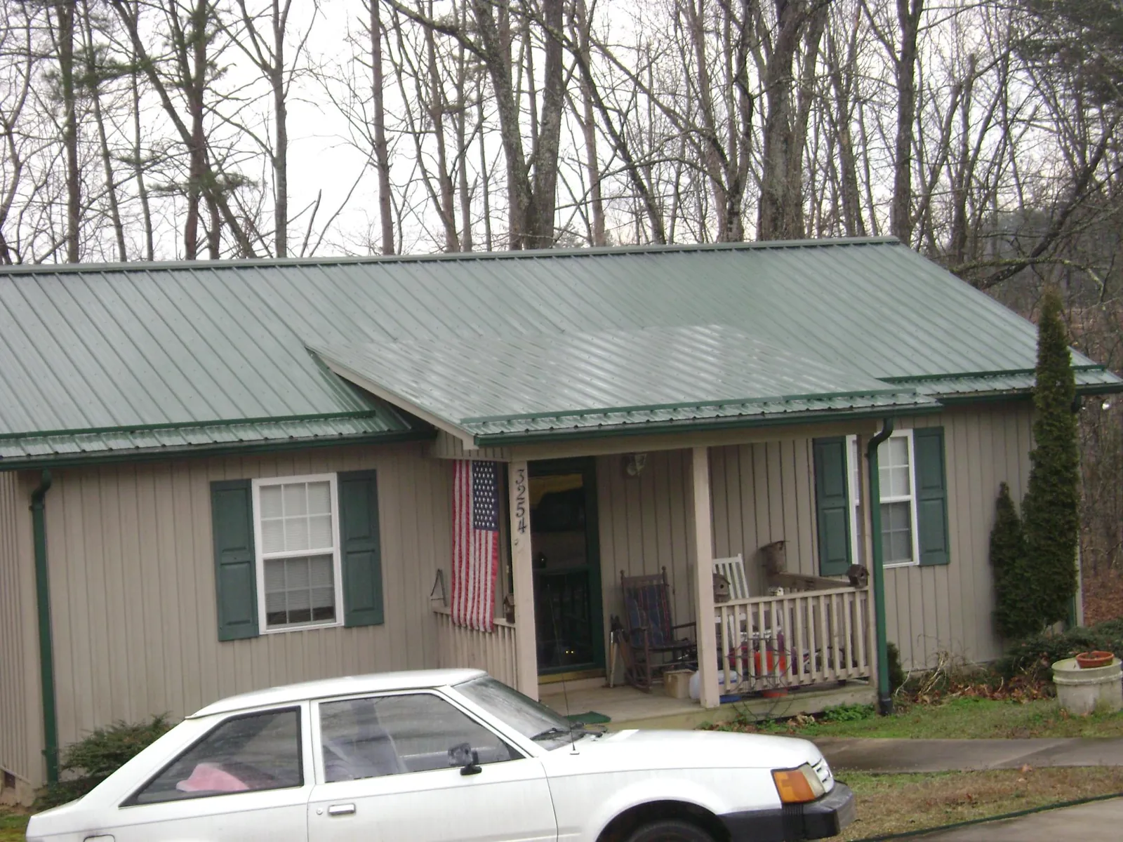 Green metal roof and front porch on a tan sided cottage in Fresh Meadows