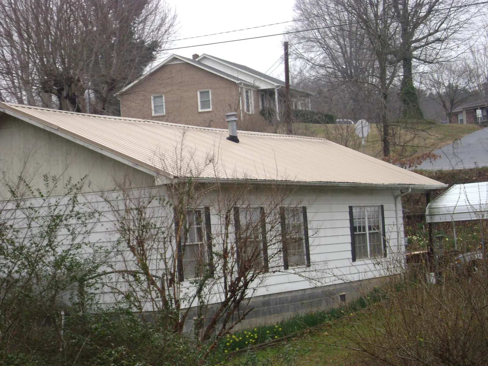 Tan metal roof on a white sided house set into a hillside — Commercial Roofing by Roofing Brothers in Fresh Meadows